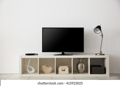 Wide Screen TV On White Stand Near Light Wall