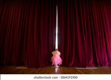 Wide shot of ballerina girl peeking through the curtains before the performance.