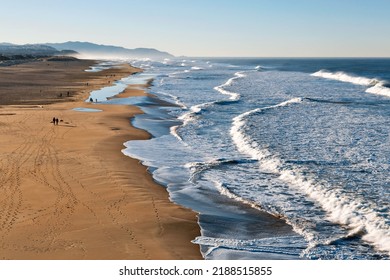 A Wide Shot Of A Beach At Morning With White Waves Washing Over The Shore