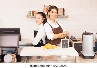 Wide Shot Of Beautiful Caucasian And Asian Barista Women Stand With Crossed Arms To Welcome Customers In Cafe Coffee Shop. Barista Work At Coffee Bar And Food Service Business