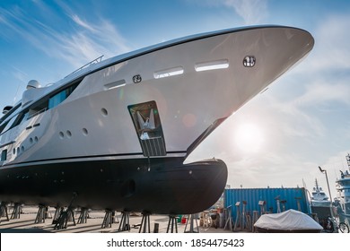 Wide shot of the bow of a new white modern superyacht on dry dock, with a bulbous bow on a sunny day, with stainless steel anchor on a sunny day with blue sky