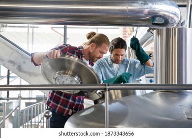 Wide Shot Of Brewery Workers Checking Fermentation Process In Steel Vat