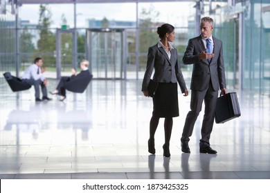 A Wide Shot Of A Businessman And Businesswoman Talking While Walking In Office Lobby.