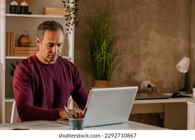 Wide shot of a busy middle aged adult man sitting at his desk in his home office using his laptop. Looking down while concentration on work. Stay at home dad and remote work concept. Copy space. - Powered by Shutterstock