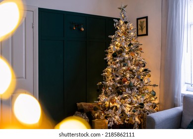 A Wide Shot Of A Christmas Tree Decorated With Golden-orange Shiny Balls And Lights In A Living Room.