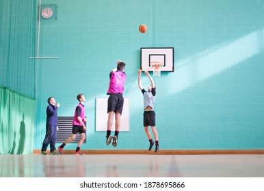 Wide Shot Of A Coach Watching High School Students Play Basketball During A Gym Class.