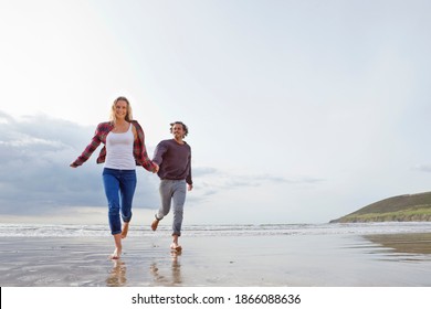 Wide Shot Of A Couple Running While Holding Hands On The Beach