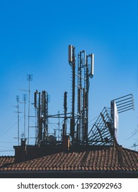 Wide shot of different aerial antennas for radio television and mobile transmission on roof tile building against blue sky