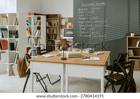 Wide shot of empty classroom displaying business English terms on chalkboard, showing migrant education, language training, financial literacy. Ideal for ESL courses, adult learning marketing