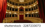 Wide shot of an Empty Elegant Classic Theatre with Red Velvet Chairs and Curtains. Well-lit Opera House with Beautiful Mural Paintings Ready to Recieve Audience for a Play or Ballet Show