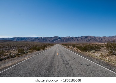 A wide shot of an empty road leading towards a mountain in the Mojave Desert