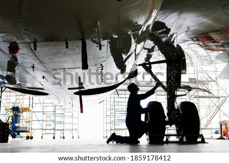 Wide shot of an engineer inspecting the landing gear of a passenger jet at a hangar.
