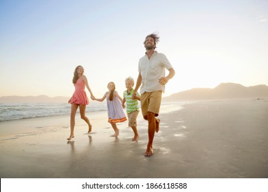 Wide Shot Of A Family Holding Hands And Running Along The Shore Of A Sunny Beach.