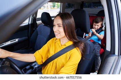 Wide Shot Of Female Driving Car With Son Sitting In Baby Seat