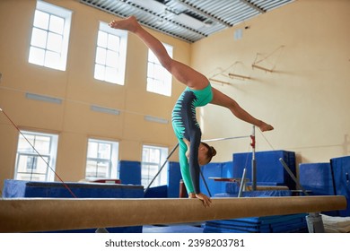 Wide shot of female gymnast doing handstand split on balance beam in gym, copy space - Powered by Shutterstock