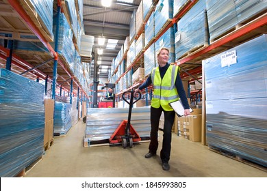 A wide shot of a female warehouse manager holding a clipboard and pulling a pallet truck. - Shutterstock ID 1845993805