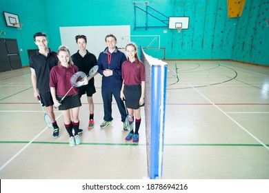 Wide Shot Of A Gym Teacher And High School Students Standing Next To A Badminton Net In A Gym.