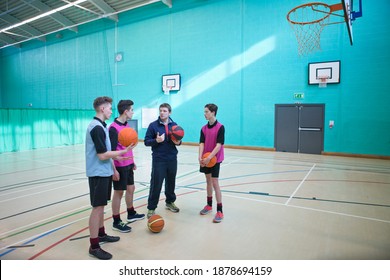 Wide Shot Of A Gym Teacher Teaching Basketball To A Group Of High School Students In A Gym.