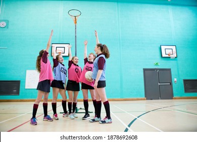 Wide Shot Of High School Girls With A Netball Raising Their Hands In A Huddle Before A Game.