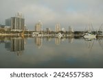 Wide shot Looking north from Demens Landing Park over smooth water with reflections towards city scape of St. Petersburg, Florida . Sailbots in marina with Cloudy blue and white sky with light fog.