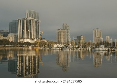 Wide shot Looking north from Demens Landing Park over smooth water with reflections towards city scape of St. Petersburg, Florida . Sailbots in marina with Cloudy blue and white sky with light fog.