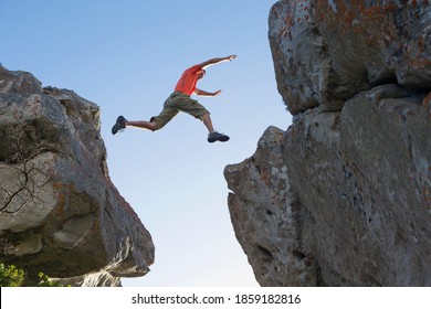 Wide shot of a male rock climber leaping between rocks.
