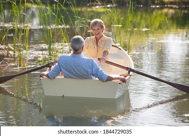 Wide shot on a happy elderly woman rowing a boat with her husband over a lake with tall grass.