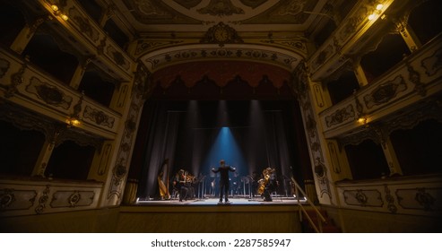 Wide shot of an Orchestra on a Classic Theatre Stage: Professional Conductor Directing Symphony Orchestra with Performers Playing Violins, Cellos, and Trumpets During Music Concert. Audience's POV