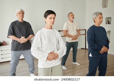 Wide shot of senior people doing breathing exercise during qigong class while pressing hands to stomach - Powered by Shutterstock