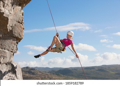 Wide shot of the side view of a female rock climber abseiling down a rock face.