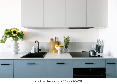 Wide shot of simple interior design in kitchen with integrated household appliances and blue modern furniture with drawers. Ceramic vases, wooden boards and set of knives on white clean countertop. - Powered by Shutterstock