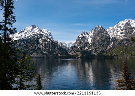 a wide shot of snow capped mountain chain facing a clear blue lake 