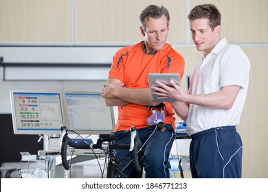 Wide shot of a sports scientist explaining a senior man sitting on an exercise bike some fitness data in a laboratory - Powered by Shutterstock