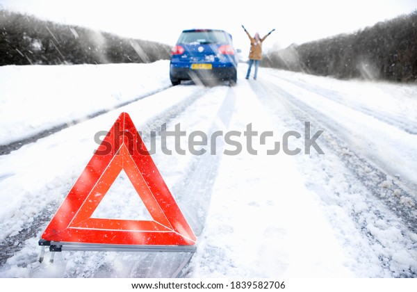 Wide shot of a stranded woman is trying to flag down\
another car next to her broken down car on a cold, snowy day to\
help her out.