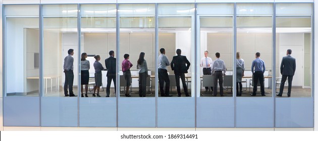 Großer Schuss durch ein Bürofenster mit einer Gruppe von Leuten, die an einem Treffen teilnehmen. – Stockfoto