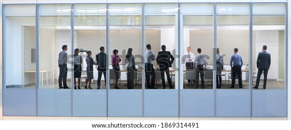 Wide shot through an office window with a group\
of people attending a\
meeting.