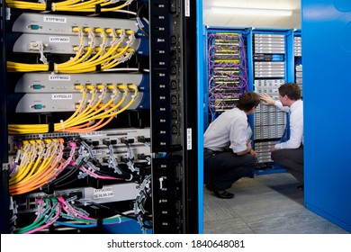 Wide shot of two IT technicians in the server room crouched down for checking network system with a server rack in the foreground
