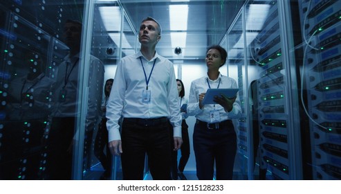 Wide shot of workers in a data center walking between rows of server racks on their way to a meeting