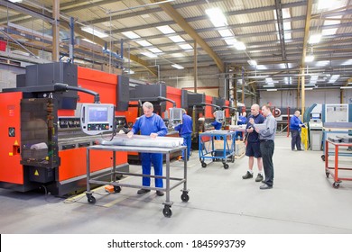A wide shot of the workers working on the machines while a managers watches them in a factory.