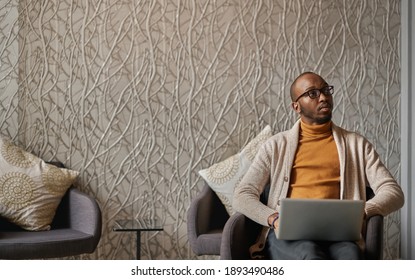 Wide Shot Of Young Motivated Black African Business Man Sitting In Office Lobby Working On Laptop Looking Into Distance With Copy Space