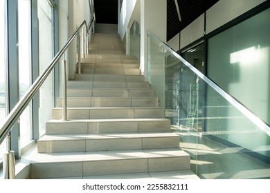 A wide staircase along the large windows in an office building. Modern interior of the lobby of an office building with large spacious windows. Illuminated long corridor in a modern business center - Shutterstock ID 2255832111