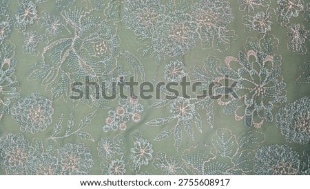 A wide, top-down view of a repeating floral embroidery pattern on a pastel green textile. The fabric showcases various sizes of embroidered blossoms and leaves in a light, shimmering thread.