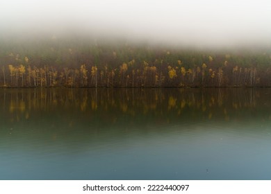 Wide Vag River Calm Autumnal Waters With Reflected Yellow And Red Deciduous Misty Forest Near Sutovo Settlement, Slovak Republic. Moody Weather And Traveling Concept.