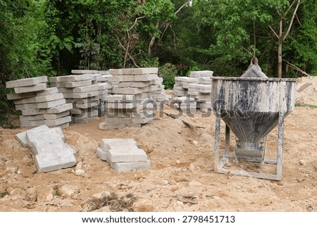 Wide view of an active construction site featuring a concrete mixer and stacks of concrete blocks on orange excavated soil. Ideal for civil engineering, residential development and infrastructure concepts.