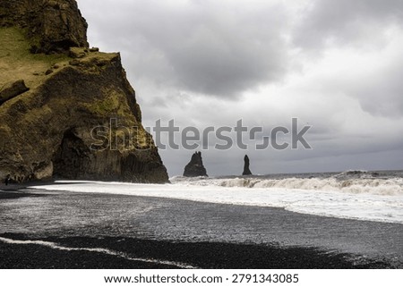 Wide view of basalt cliffs and sea stacks at black sand beach under overcast sky in Vik South Coast Iceland