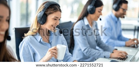 Wide view of beautiful blonde girl with coffee cup working on computer accompanied with group of call center operators.