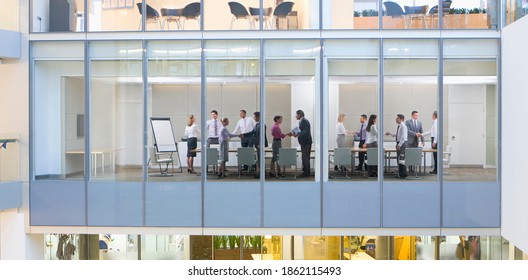 A Wide View Of Business People Meeting And Shaking Hands With Each Other In A Conference Room Seen Through The Glass Walls From Outside Of A Modern Building