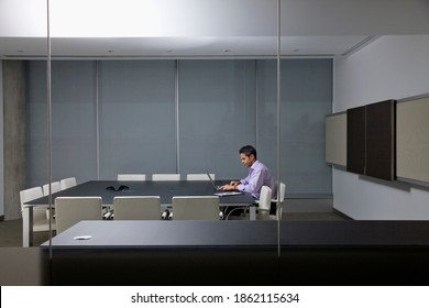 A wide view of a businessman working alone on a laptop till late in the conference room