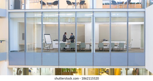 A Wide View Of Businessmen Shaking Hands In A Conference Room From Outdoors Through A Glass Wall