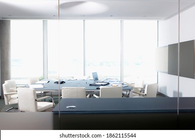 A wide view of a conference room through a glass wall with laptop and papers lying on the table
